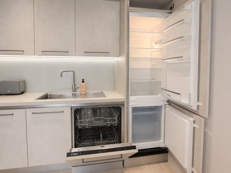 Modern white kitchen with dishwasher, sink, and open refrigerator door