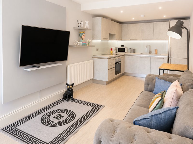 Open-plan living kitchen with beige cabinetry, wall-mounted TV, sofa, and wooden flooring