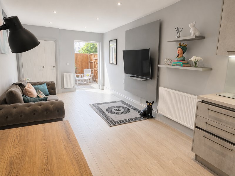 Modern living room with brown sofa, TV wall, wooden floors, and door to garden