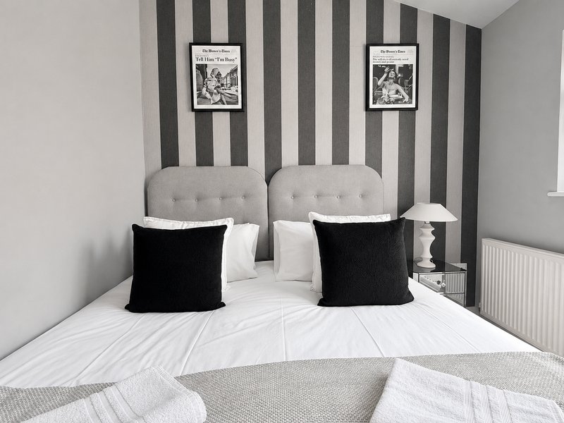 Modern bedroom with two upholstered headboards, black cushions, striped wallpaper, and white bedding