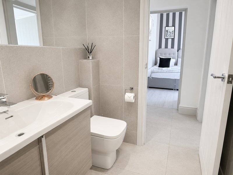 Modern bathroom with white vanity, toilet, mirror and beige tile walls