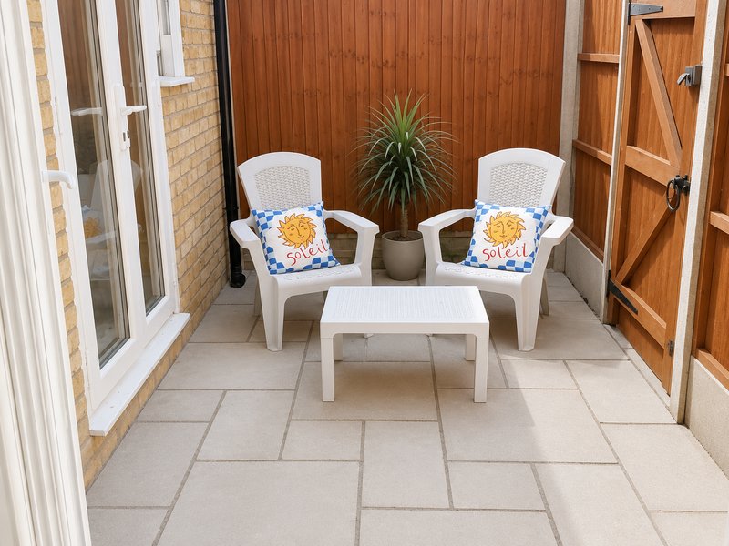 Patio seating area with two white chairs, small table, potted plant and wooden doors