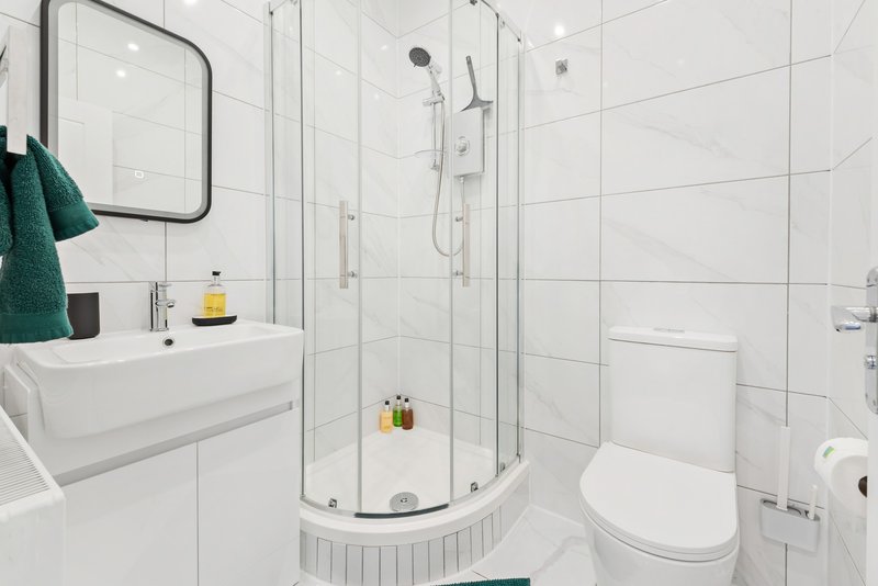 Modern white bathroom with shower enclosure, sink, toilet, and teal towel