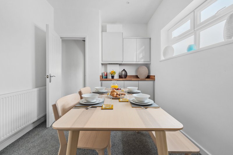 Bright dining room with wooden table, place settings, and kitchen counter with decorative items