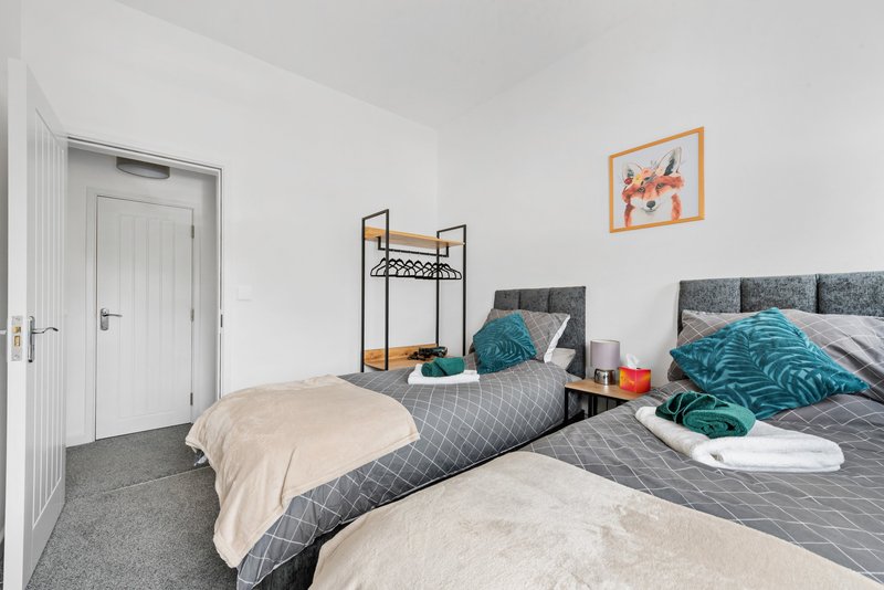 Bright bedroom with two single beds, grey bedding, teal pillows and throws, wooden nightstand. Can be made in to a king bed.