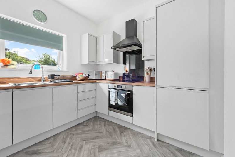 Modern kitchen with white cabinetry, black range hood, built-in oven and window overlooking garden