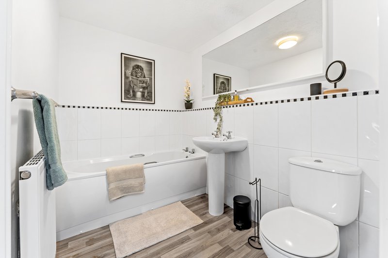 Modern bathroom with white tile, pedestal sink, toilet, bathtub and wooden floor.