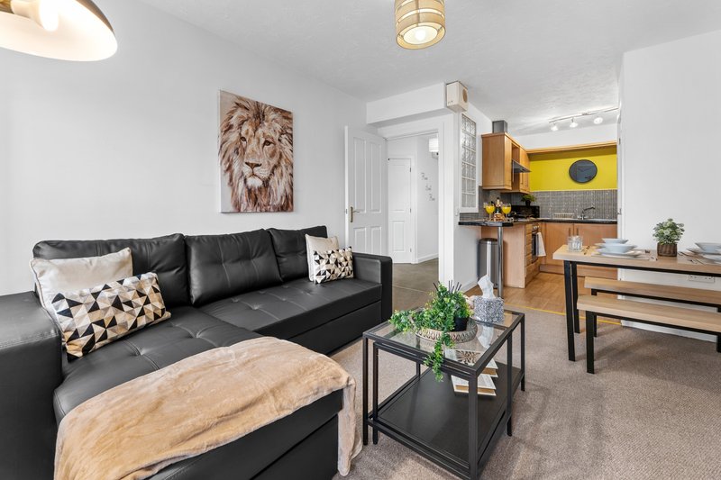 Open-plan living area with black sofa, wooden coffee table, lion wall art, and kitchenette with yellow accent wall