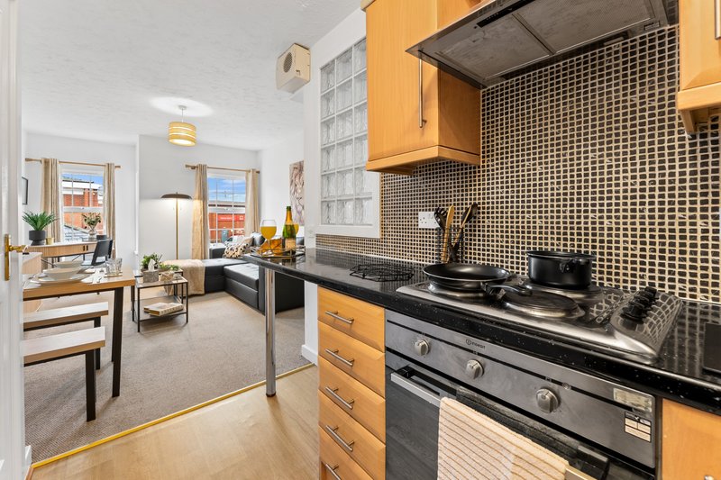 Modern kitchen with yellow cabinets, black countertop, and open-plan living area beyond
