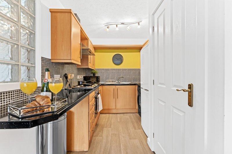Galley kitchen with wooden cabinets, yellow walls, black countertop and stainless steel appliances
