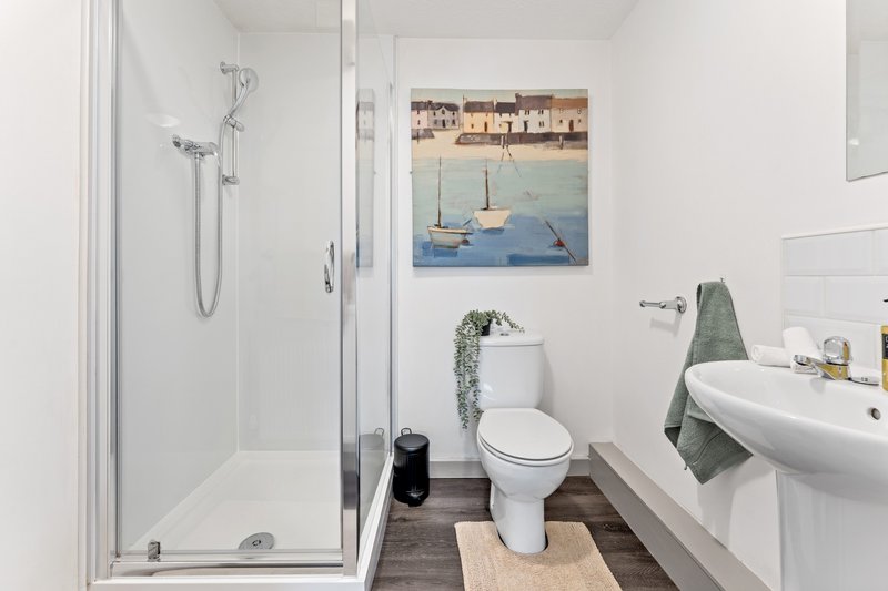 Clean bathroom with shower enclosure, toilet, pedestal sink and framed coastal artwork