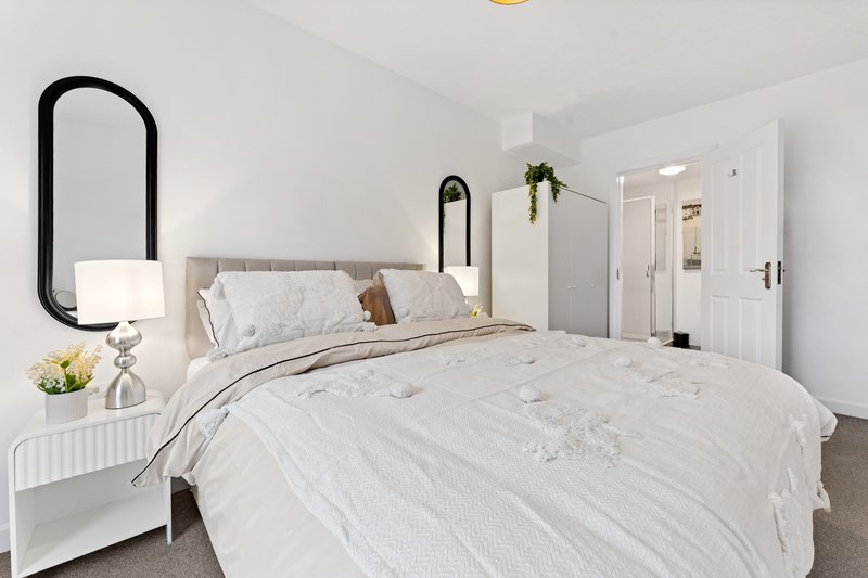 Bright bedroom with white bedding, upholstered headboard, black mirror and white nightstand