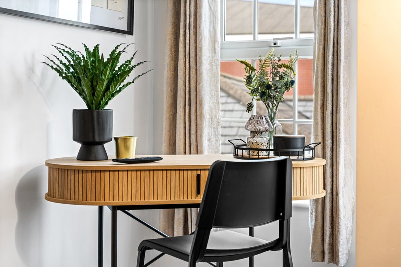 Modern desk workspace with wooden drawers, black chair, potted plant and flowers by window