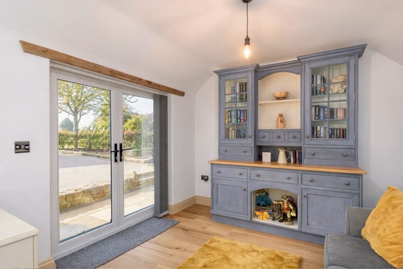 Bright living room with blue built-in shelving, wooden beams, glass doors to garden, and yellow accent cushion.
