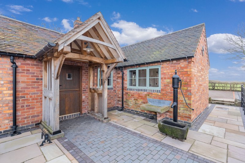 Brick cottage exterior with timber porch, paved courtyard and clear blue sky