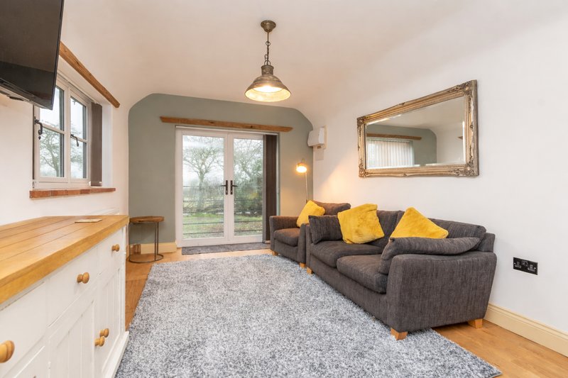 Modern living room with Smart TV, gray sofa, yellow cushions, wooden furniture and patio French doors.