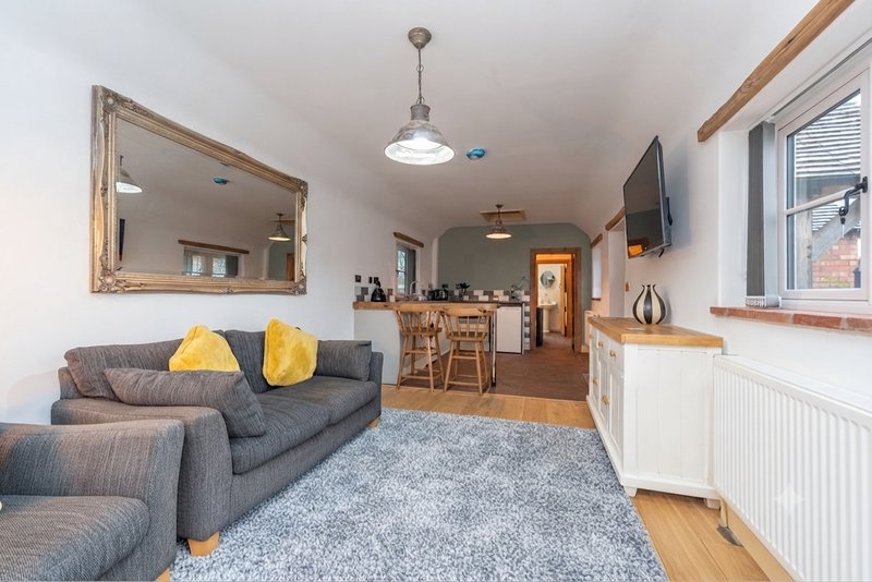 Open-plan living room with gray sofa, yellow cushions, wooden floor and fully equipped kitchen.