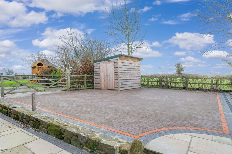 Outdoor paved parking area with storage shed, fencing, and landscaping under clear sky