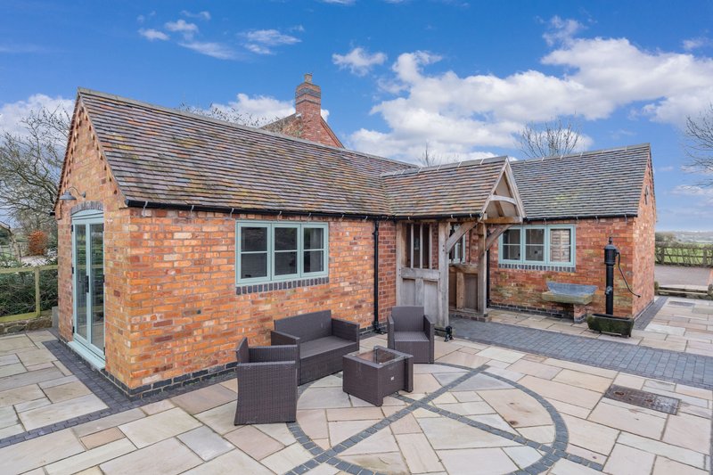 Brick countryside cottage with patio seating area and blue sky background