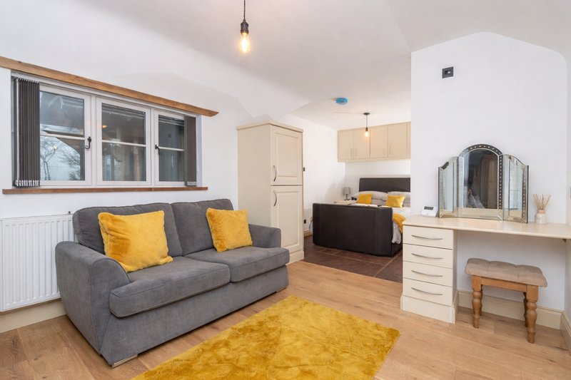 Open-plan bedroom seating room with gray sofa bed, yellow accents, wooden flooring and dressing table/ desk.