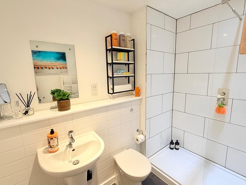 Clean bathroom with white subway tiles, round sink, toilet, and shower enclosure with shelving