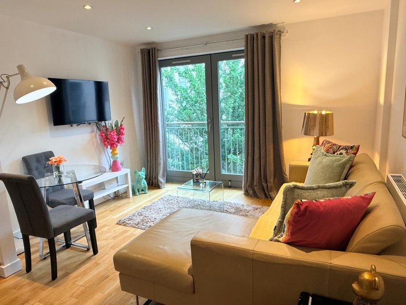 Modern living room with sofa, armchair, TV, desk and glass doors opening to balcony