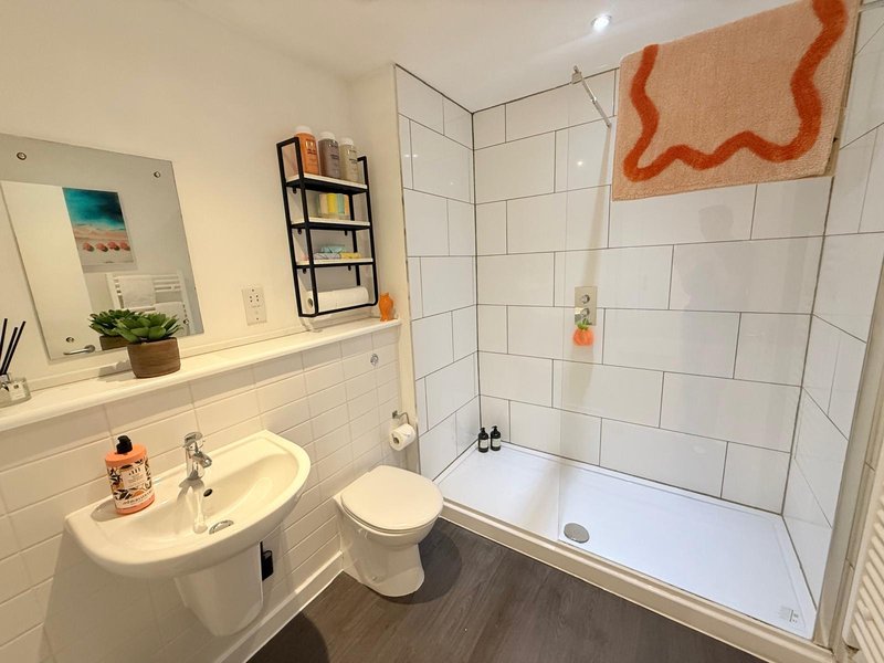 Modern bathroom with white tile walls, sink, toilet, shower enclosure and orange towel