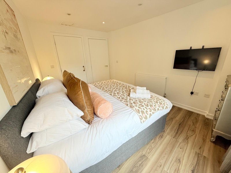 Modern bedroom with double bed, decorative pillows, wall-mounted TV and wooden flooring