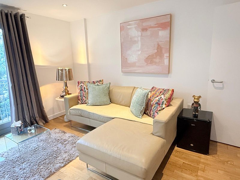 Modern living room with cream sectional sofa, colorful cushions, wooden floor and artwork