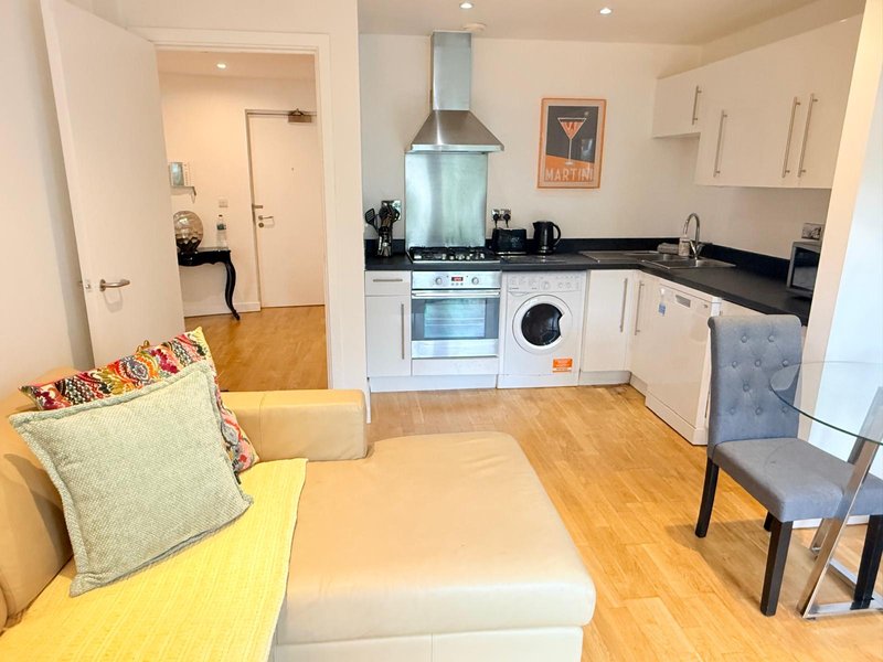 Open-plan kitchen and living area with white cabinetry, wooden flooring, and cream upholstered seating