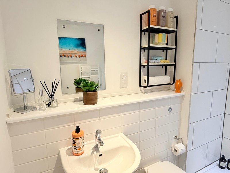 Clean modern bathroom with white tile walls, sink, mirror, shelving and decorative items
