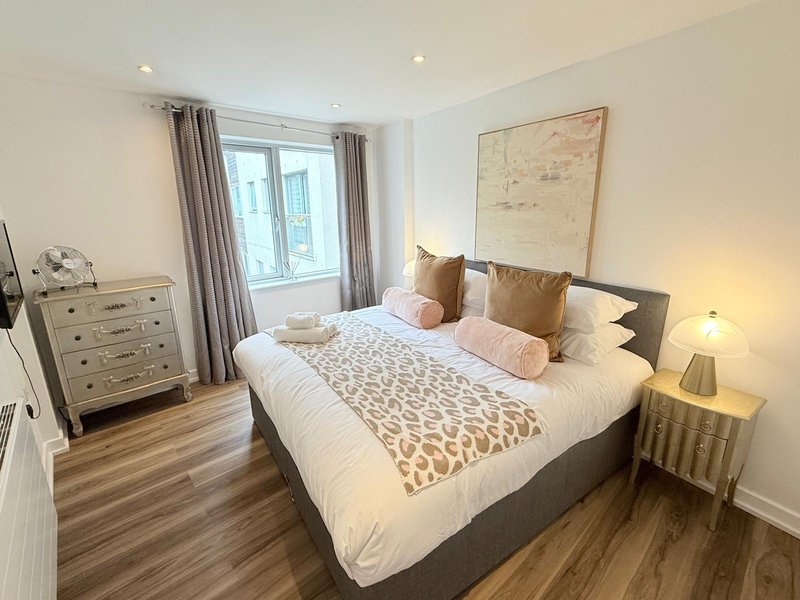 Bright modern bedroom with double bed, wooden flooring, chest of drawers and window with curtains