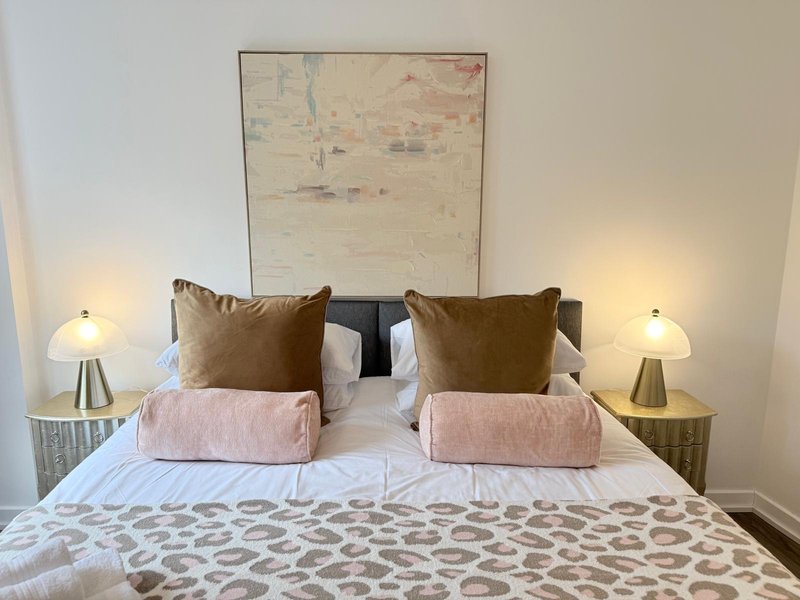 Modern bedroom with double bed, brown pillows, pink cushions, bedside lamps and framed artwork