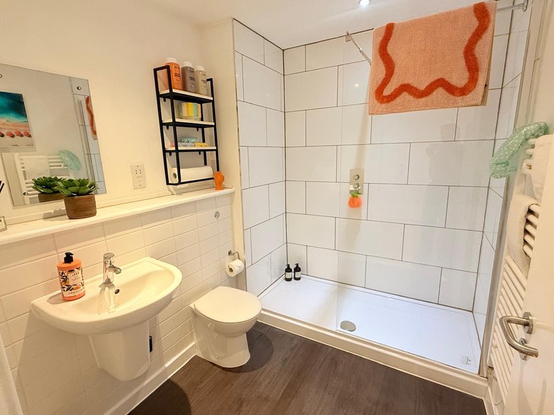 Modern bathroom with white tile walls, sink, toilet, shower enclosure and orange towel