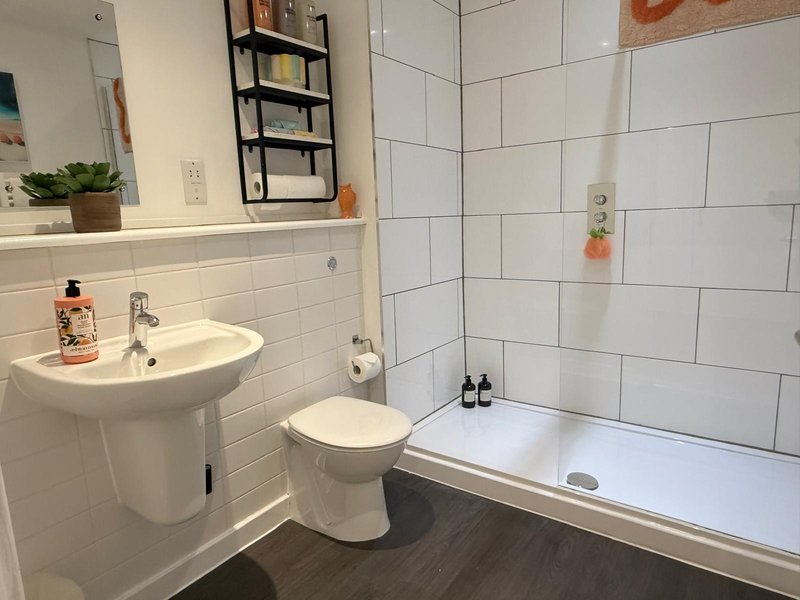 Clean modern bathroom with white subway tiles, pedestal sink, toilet, and bathtub with shower screen