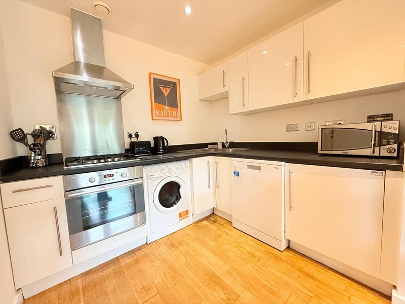 Modern kitchen with white cabinets, black countertops, integrated appliances and wooden floor