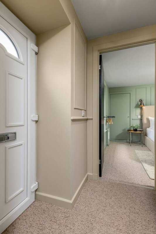 Hallway with white door, beige walls, and view into green-painted bedroom beyond