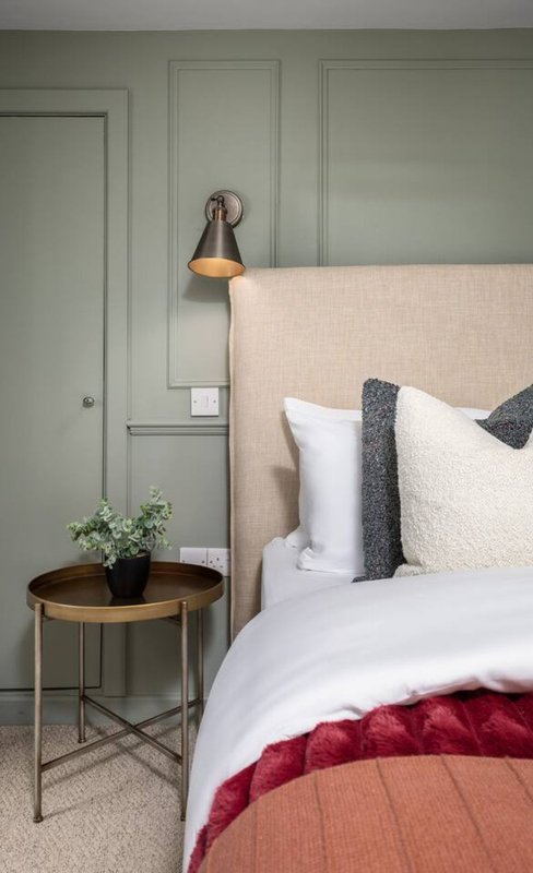 Modern bedroom with cream upholstered headboard, white bedding, burgundy throw, and brass pendant light