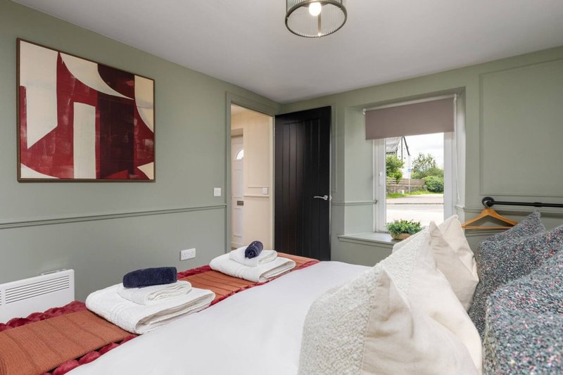 Modern bedroom with two beds, sage-green walls, abstract artwork, and glass doors to garden
