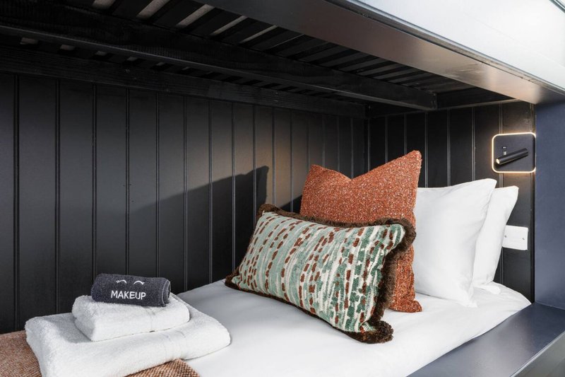 Modern bedroom with black paneled headboard, white bedding, decorative cushions and folded towels