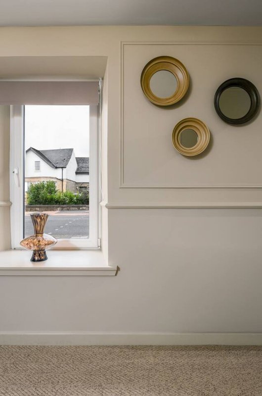 Neutral interior with window, decorative circular mirrors on wall, and small vase on sill
