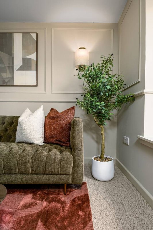 Modern living room with olive-green armchair, decorative pillows, potted plant, and abstract wall art