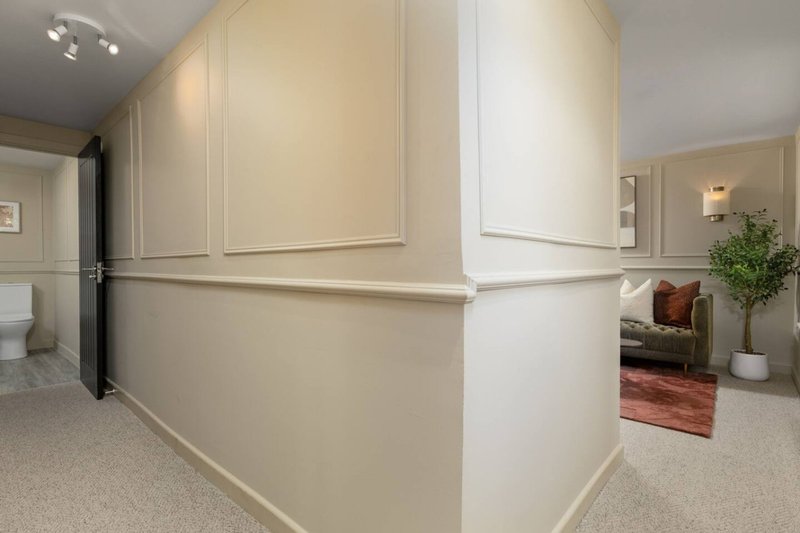 Modern hallway with cream panelled walls, carpet flooring, and open doorways to adjacent rooms