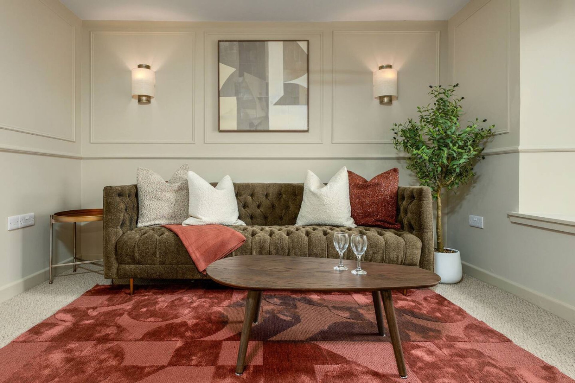 Modern living room with olive-green sofa, red patterned rug, wooden coffee table and wall art
