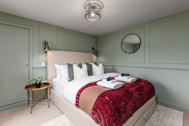 Modern bedroom with sage green panelled walls, queen bed with burgundy throw, white bedding and decorative pillows