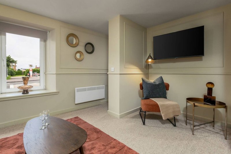 Modern living room with round marble table, wall-mounted TV, armchair, and garden view