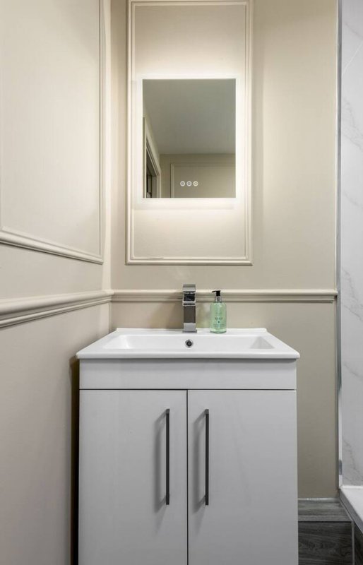 Modern bathroom with white vanity unit, sink, illuminated mirror and neutral wall paneling