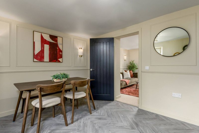 Bright hallway with dining table, wooden chairs, framed red artwork and circular mirror
