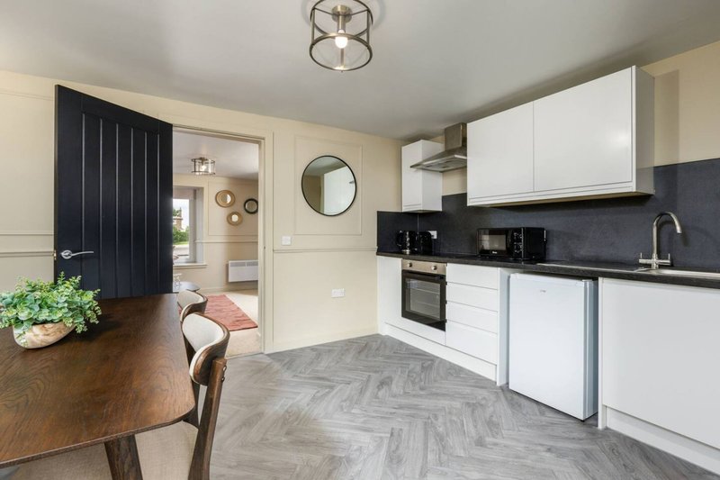 Modern kitchen with white cabinetry, black backsplash, and dining area with wooden table