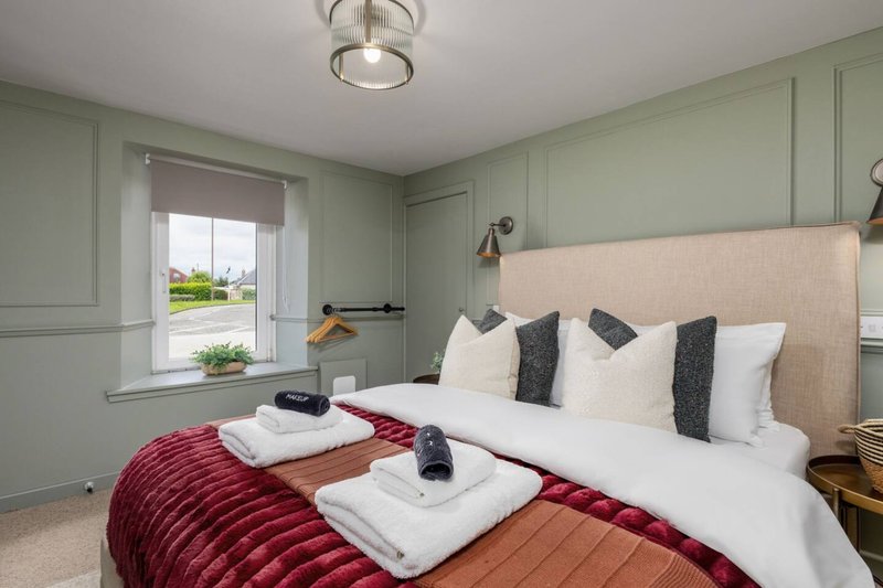Bedroom with dual beds, cream headboard, red quilts, sage green walls and window